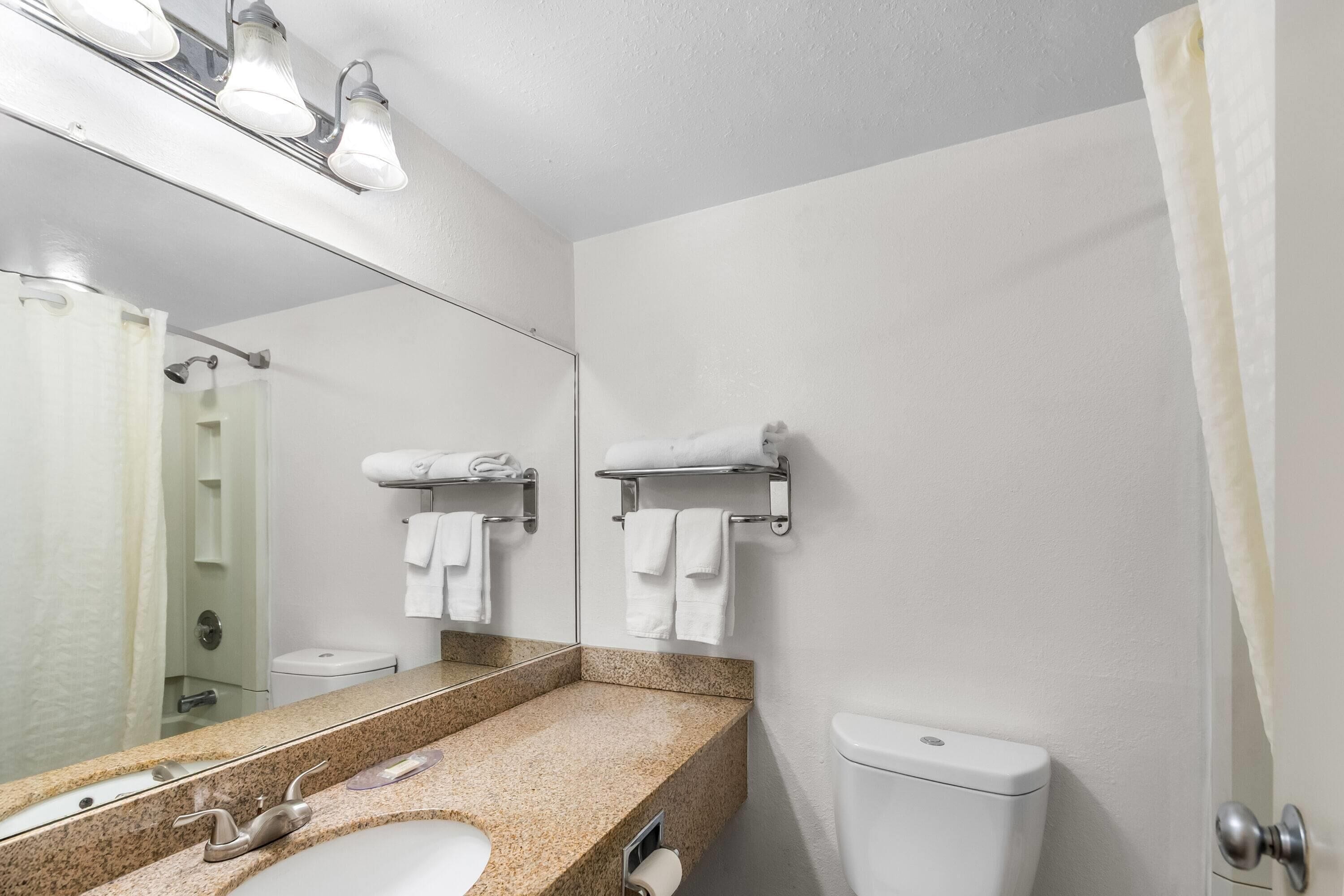 Et badeværelse med vaskebord i granit, toilet, brusebad og et spejl med lys.