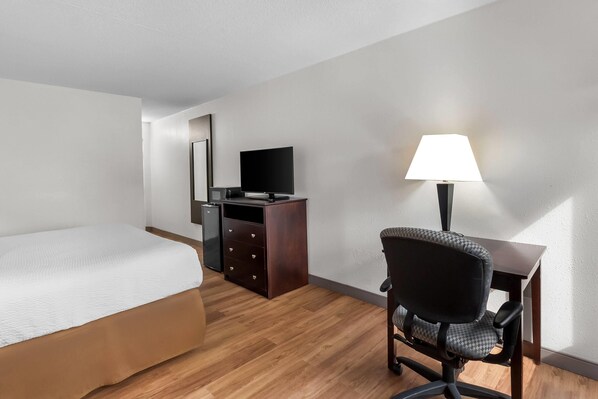 Una habitación de hotel con una cama, un escritorio con lámpara, un televisor y un aparador.