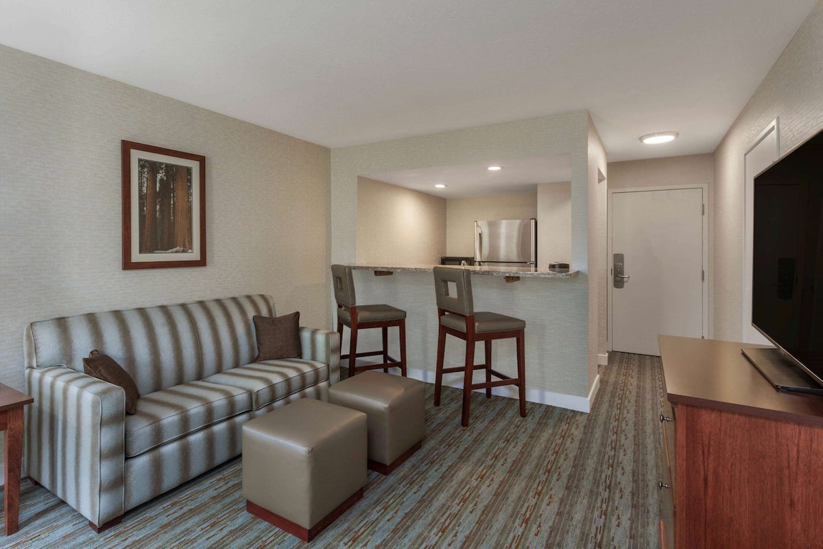 Quarto de hotel com sofá, duas cadeiras, televisão, frigorífico e uma porta.