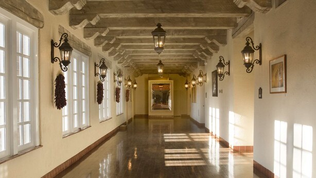 A long, well-lit hallway with decorative wall sconces, a polished wooden floor, and a central doorway. - Hilton Santa Fe Historic Plaza (Santa Fe)