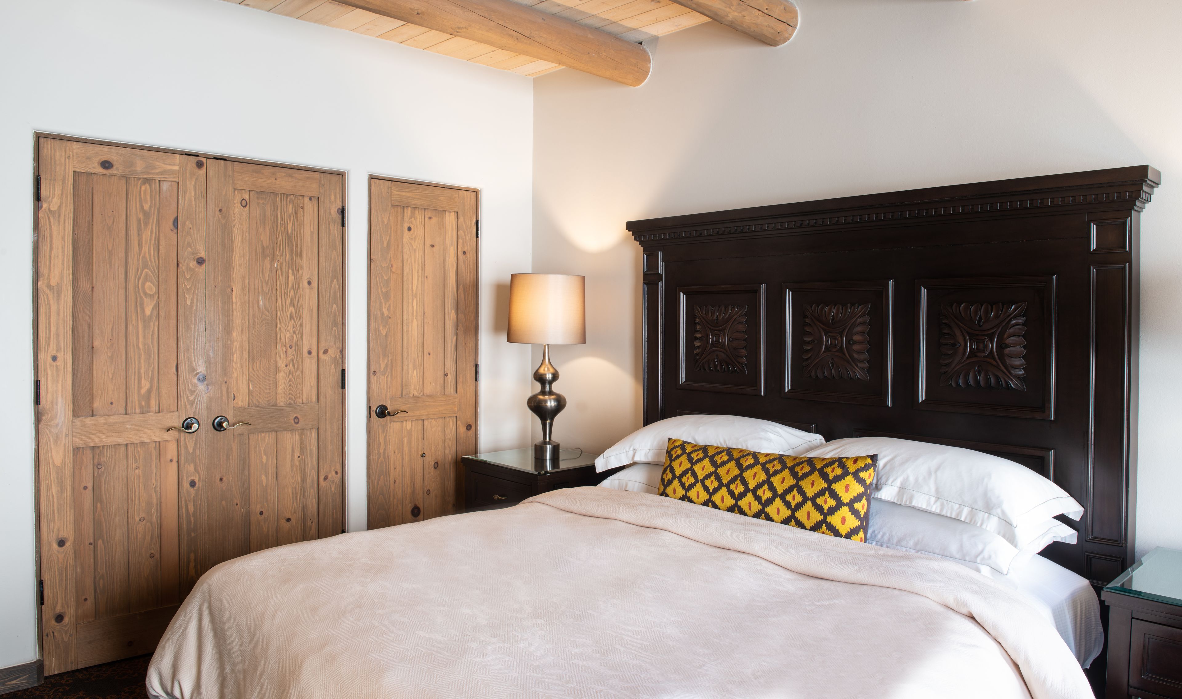 Een slaapkamer met een groot bed, een houten garderobe en een nachtkastje met een lamp.