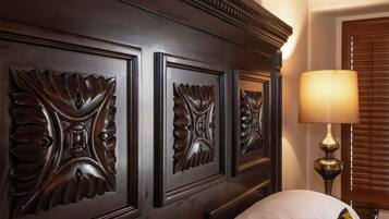 A bedroom with a dark wood headboard featuring ornate leaf carvings, a bedside lamp, and a white pillow.