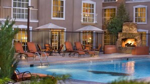 A poolside area with lounge chairs and umbrellas, a stone fireplace, and a building with large windows. - Hilton Santa Fe Historic Plaza (Santa Fe)