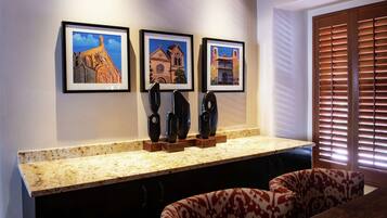 A kitchen with a granite countertop, three framed paintings, and a window with blinds.