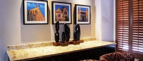 A kitchen with a granite countertop, three framed paintings, and a window with blinds.