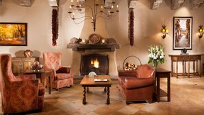 A cozy living room with a fireplace, patterned armchairs, a wooden coffee table, and a chandelier. - Hilton Santa Fe Historic Plaza (Santa Fe)