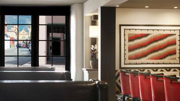 A hotel lobby with a large window, a wall-mounted abstract painting, and red chairs.