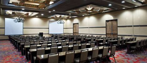 A conference room with rows of chairs and tables, a projector screen, and a large screen.
