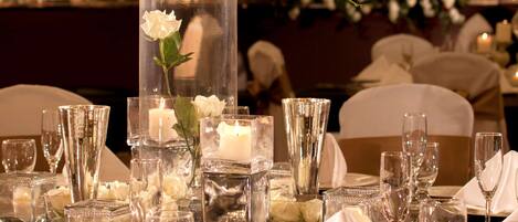 A table set for a formal event with a tall vase of white flowers, candles, and clear glassware.