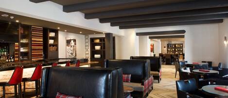 A modern bar area with leather seating, wooden bar counters, and a herringbone floor pattern.
