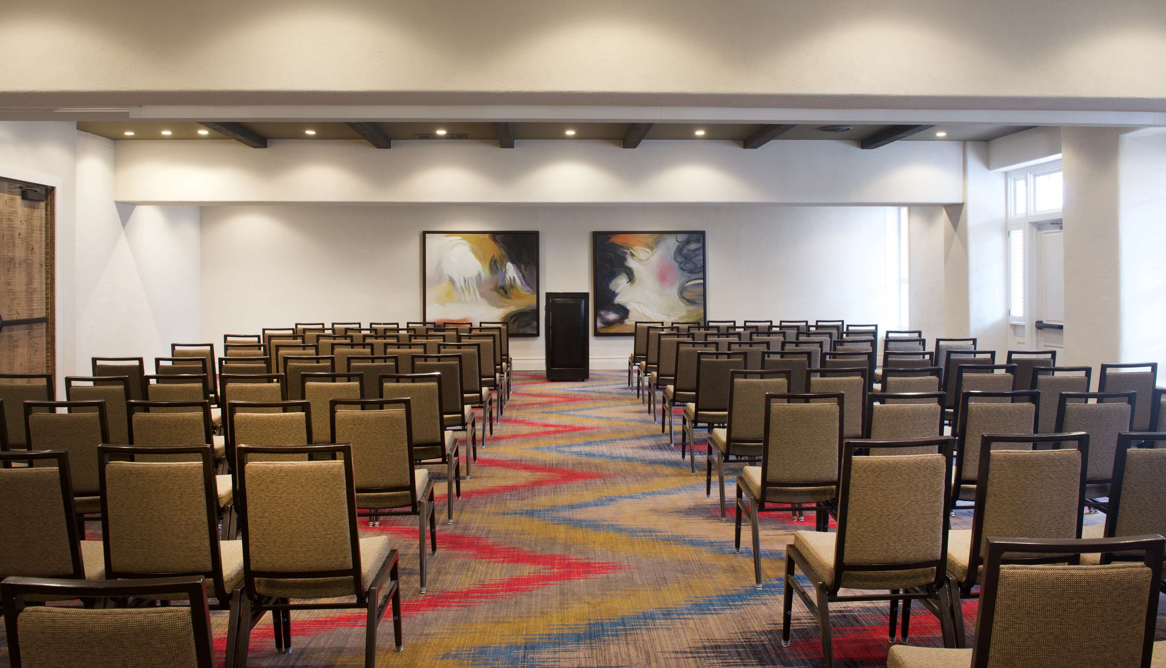 A conference room with rows of chairs, a colorful carpet, and two large abstract paintings on the walls.