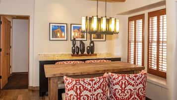 A dining area with a wooden table and patterned chairs, a chandelier, and framed pictures on the wall.
