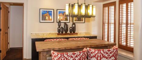 A dining area with a wooden table and patterned chairs, a chandelier, and framed pictures on the wall.