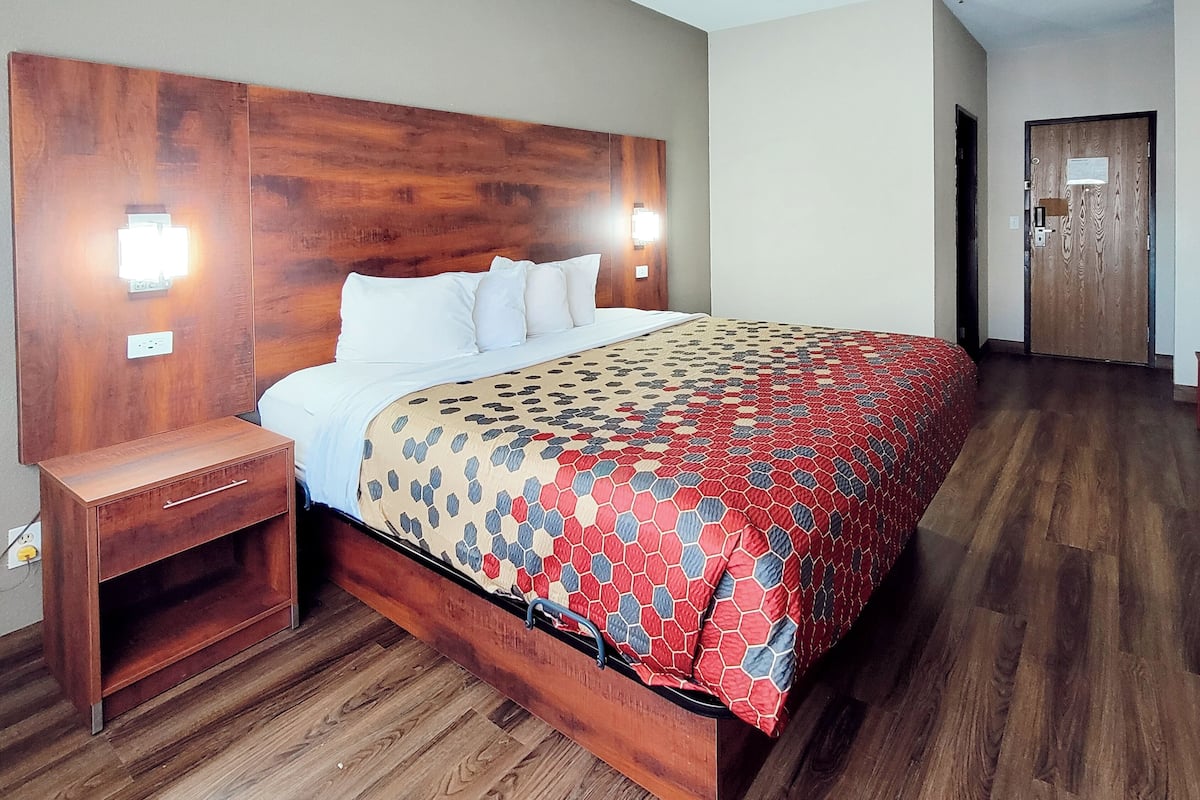 Una habitación de hotel con cabecera de madera, cama con colcha estampada, mesita de noche y suelo de madera.