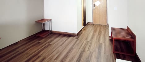 Un pasillo con suelo de madera, una mesita y una puerta.