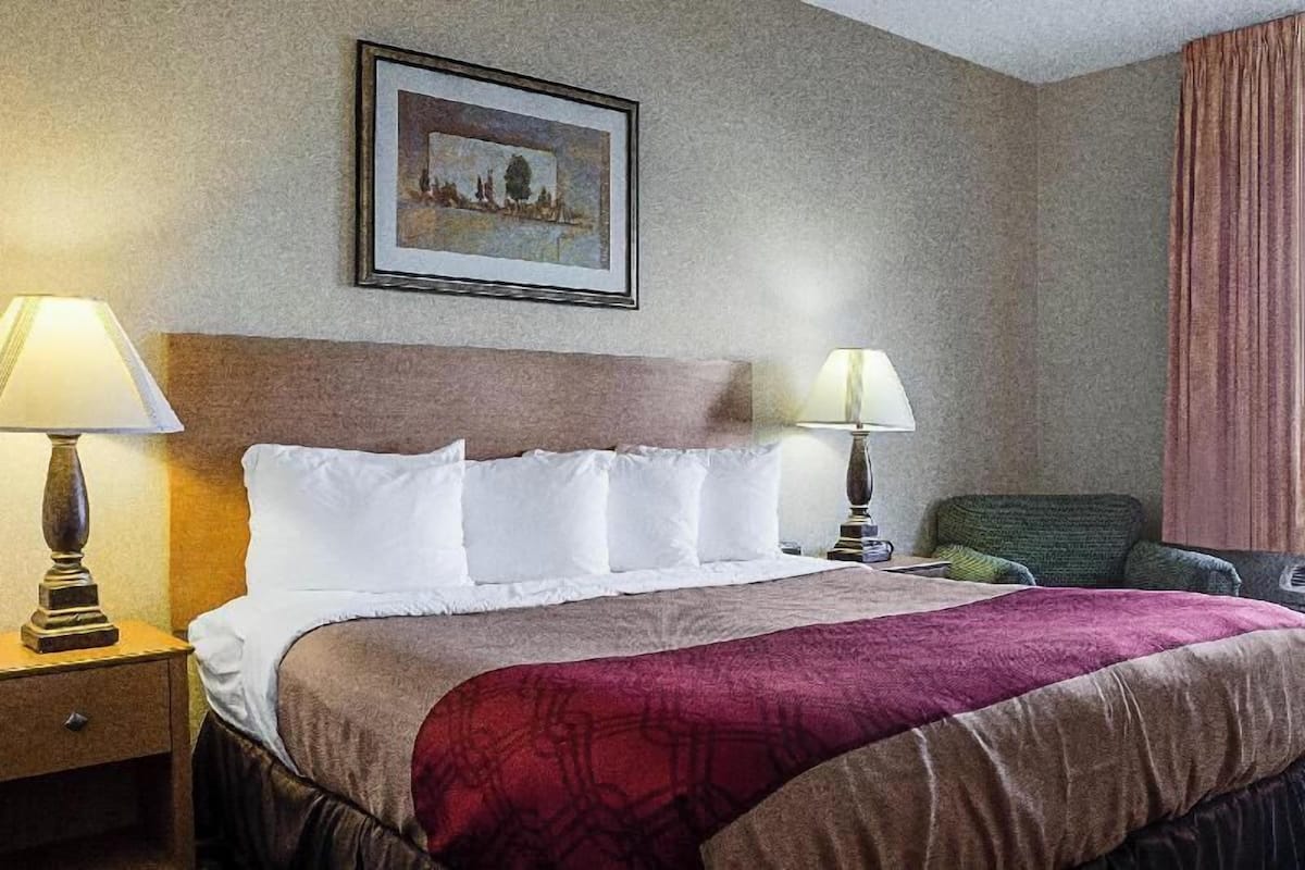 Una habitación de hotel con una cama, dos lámparas de noche, un cuadro en la pared y una silla verde.