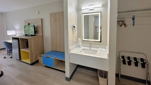 Habitación de hotel con escritorio, computadora y baño con lavamanos y espejo.