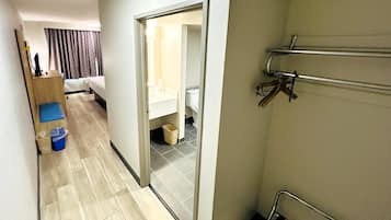 Habitación de hotel con cama, escritorio, silla, un cubo de basura azul y baño visible a través de una puerta abierta.