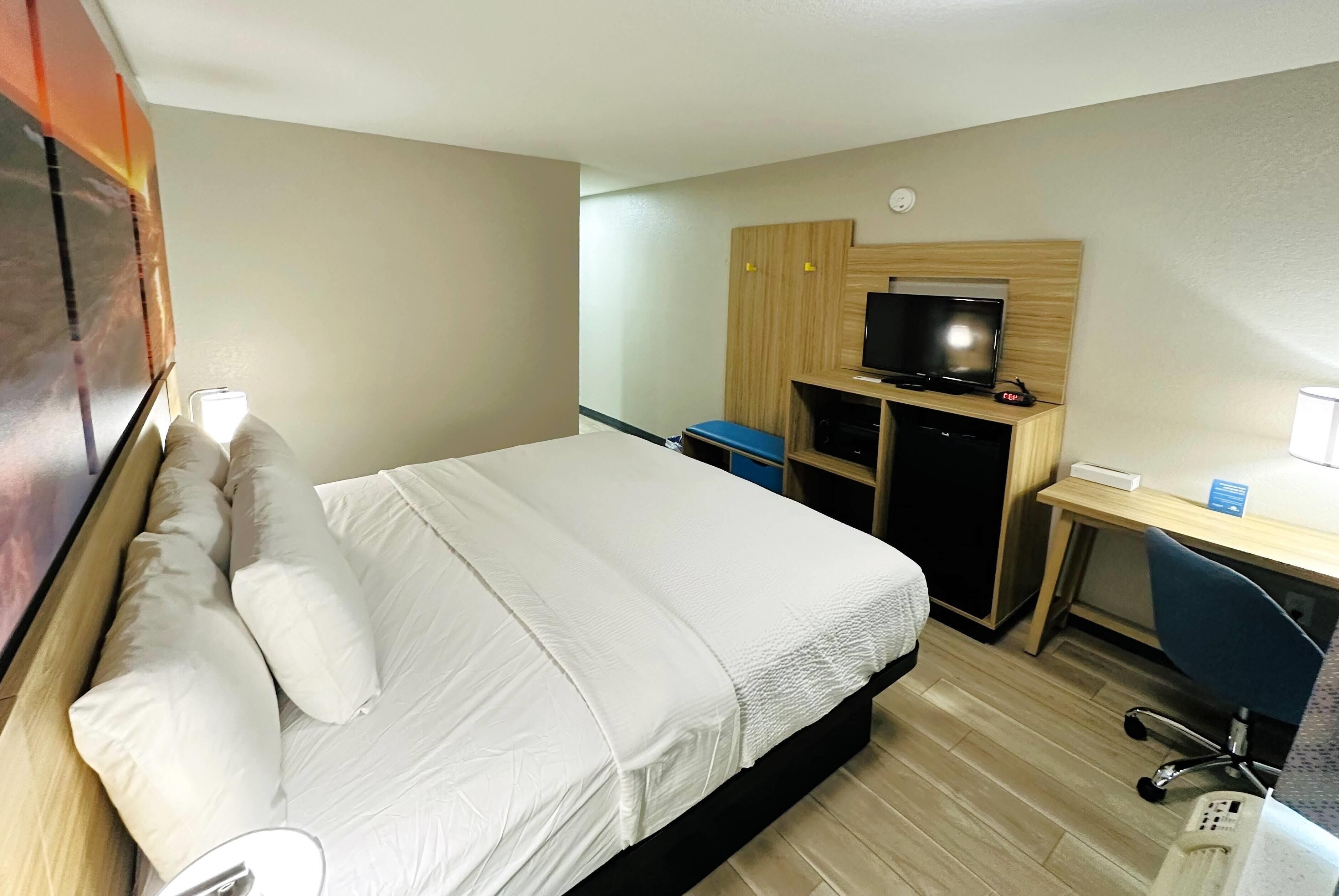 Une chambre d’hôtel comprenant un lit, un bureau avec un ordinateur, une télévision et une chaise.