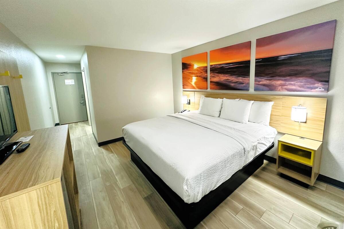 A hotel room with a large bed, a desk, and a wall with sunset paintings.