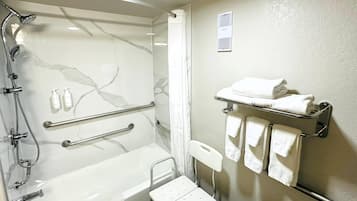 Ein Badezimmer mit Dusche, Haltegriffen, einer rollstuhlgerechten Sitzbank und einem Handtuchhalter.