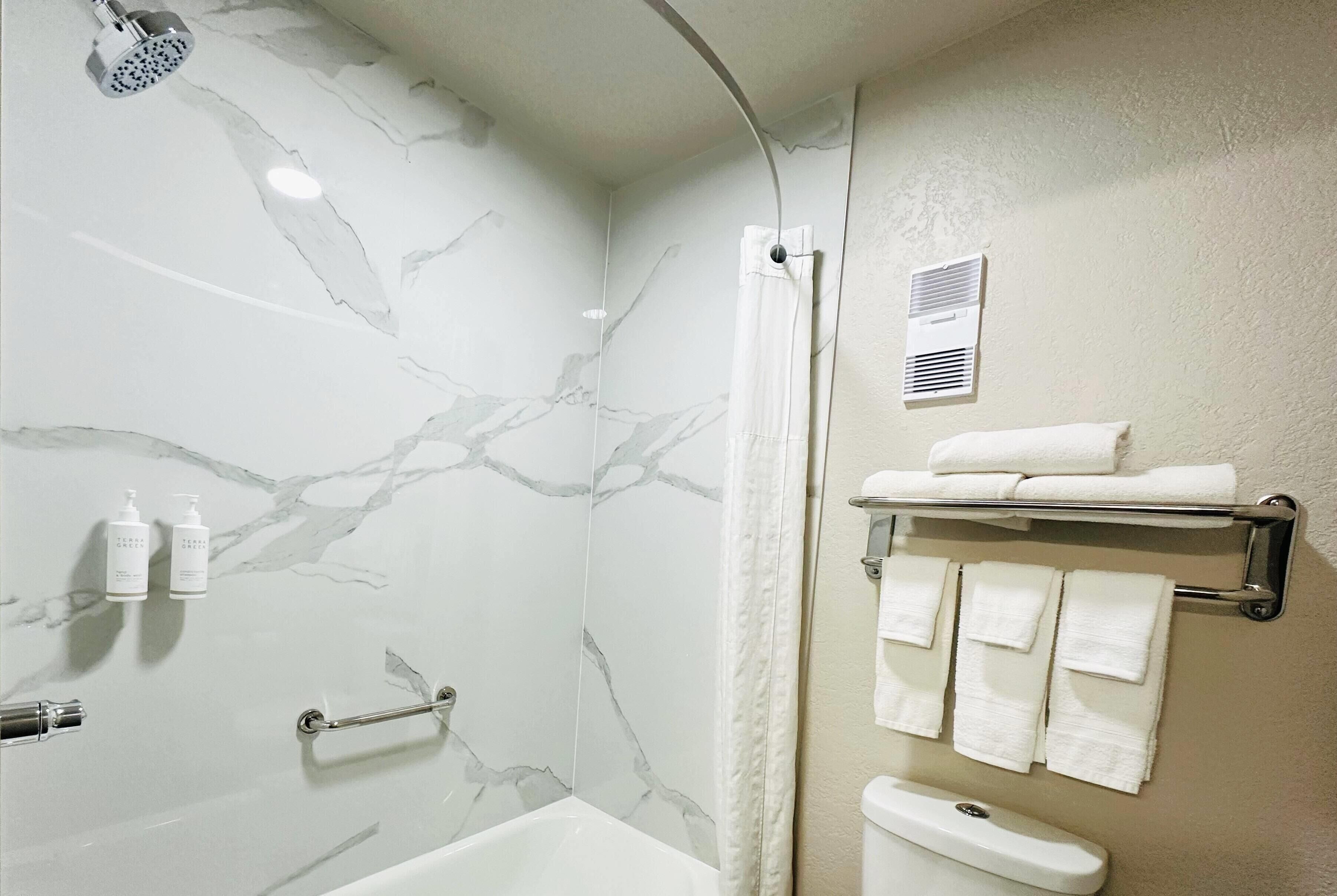 A bathroom with a bathtub, a shower, marble walls, a towel rack, and a handrail.