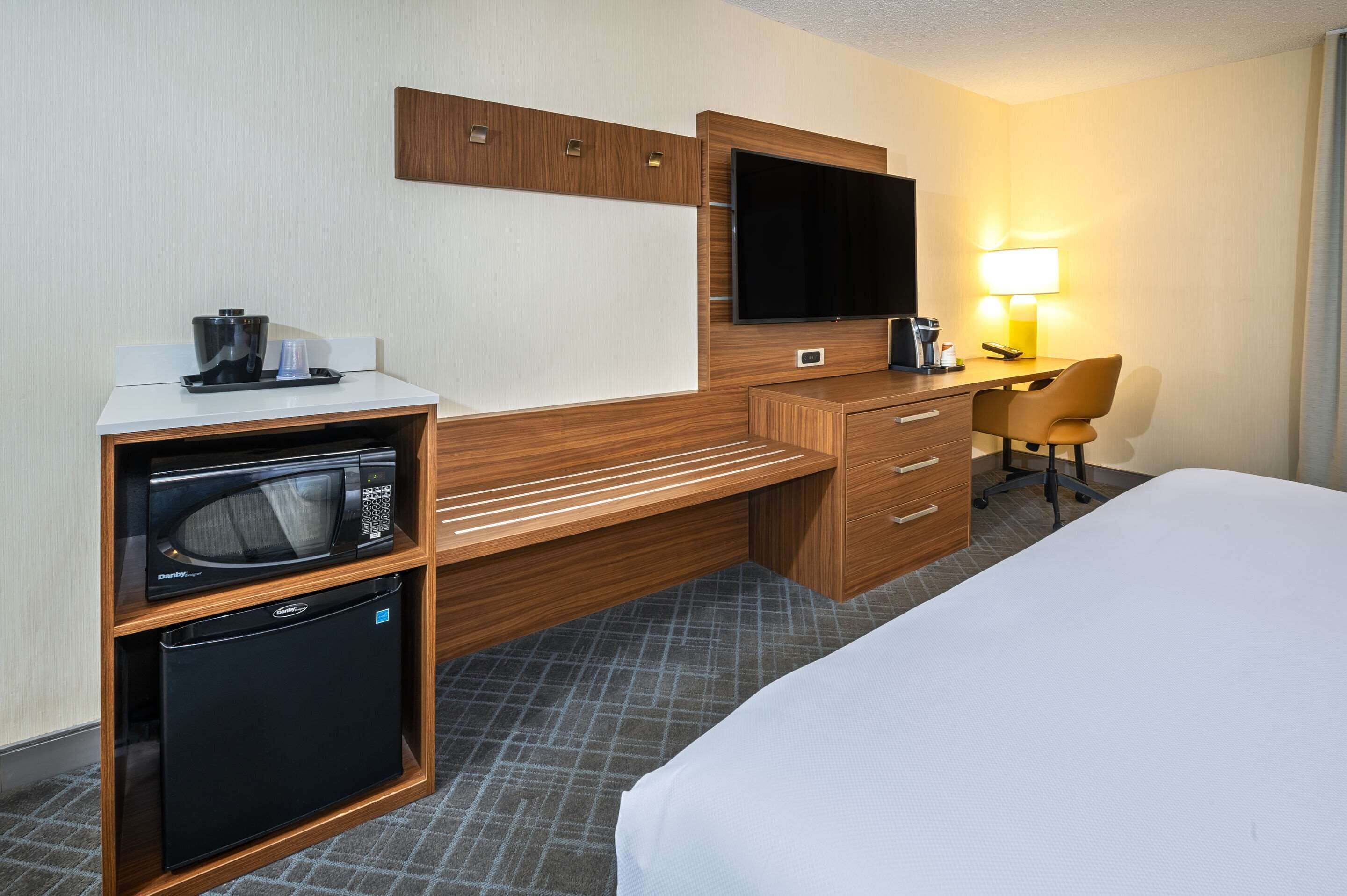 Habitación de hotel con cama, escritorio con televisor, microondas y refrigerador pequeño.