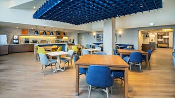 Un comedor moderno con mesas de madera y sillas azules, una cocina al fondo, y un diseño único en el techo azul.