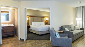 A hotel room with a bed, a sofa, a chair, a desk, and a bathroom.