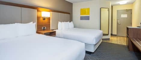 A hotel room with two beds, a wooden headboard, a nightstand, a lamp, a mirror, and a door.