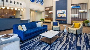 A modern lobby with a blue sofa, patterned armchairs, a coffee table, and a reception desk.