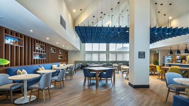 A modern restaurant with wooden panel walls, blue seating, and a high ceiling with unique lighting fixtures.
