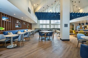 Un restaurante moderno con paneles de madera, asientos azules y un techo alto con luminarias únicas.