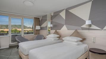 Habitación de hotel con dos camas, una silla, una mesita y vista a la ciudad.