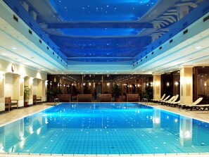 An indoor swimming pool with a tiled floor, wooden benches, and potted plants. - Ensana Thermal Margaret Island (Budapest)