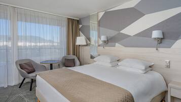 A hotel room with a large bed, a chair, a small table, and a view of the mountains.