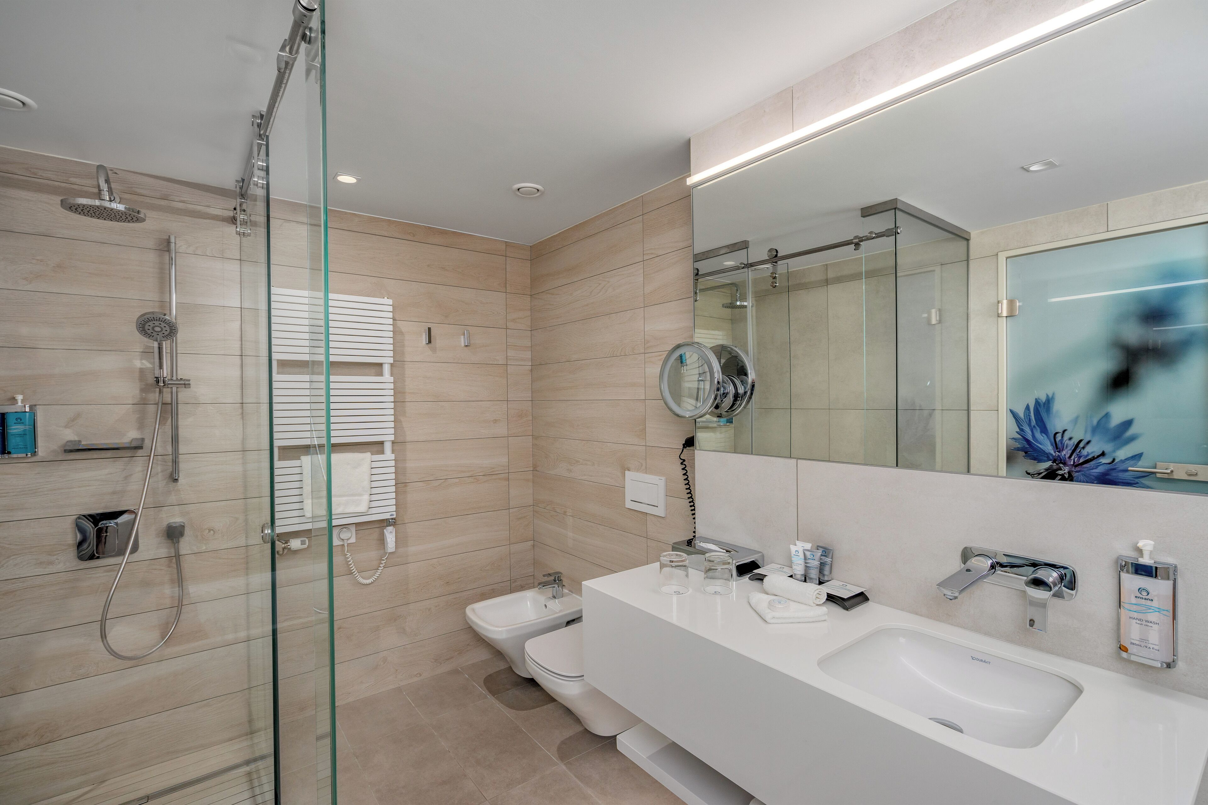 Un baño moderno con ducha de vidrio, lavamanos doble y un espejo grande.