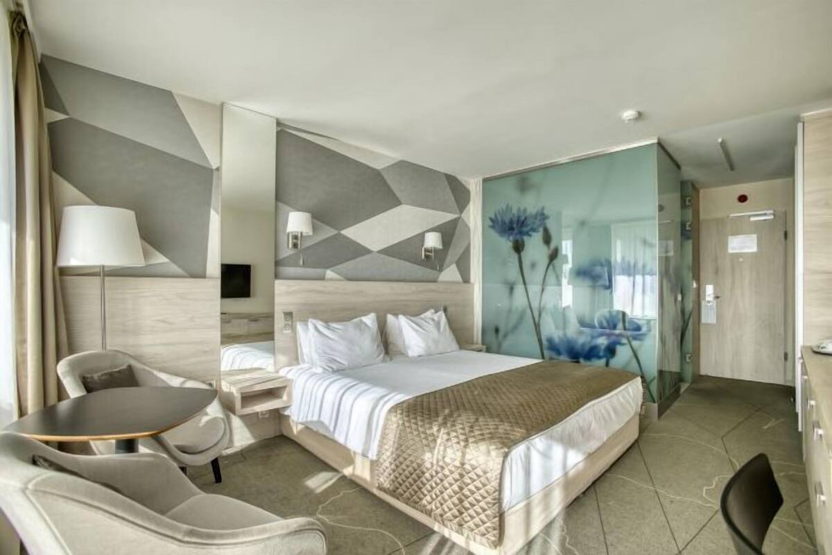Ein modernes Hotelzimmer mit Bett, Schreibtisch, Stuhl und einer Glastrennwand.