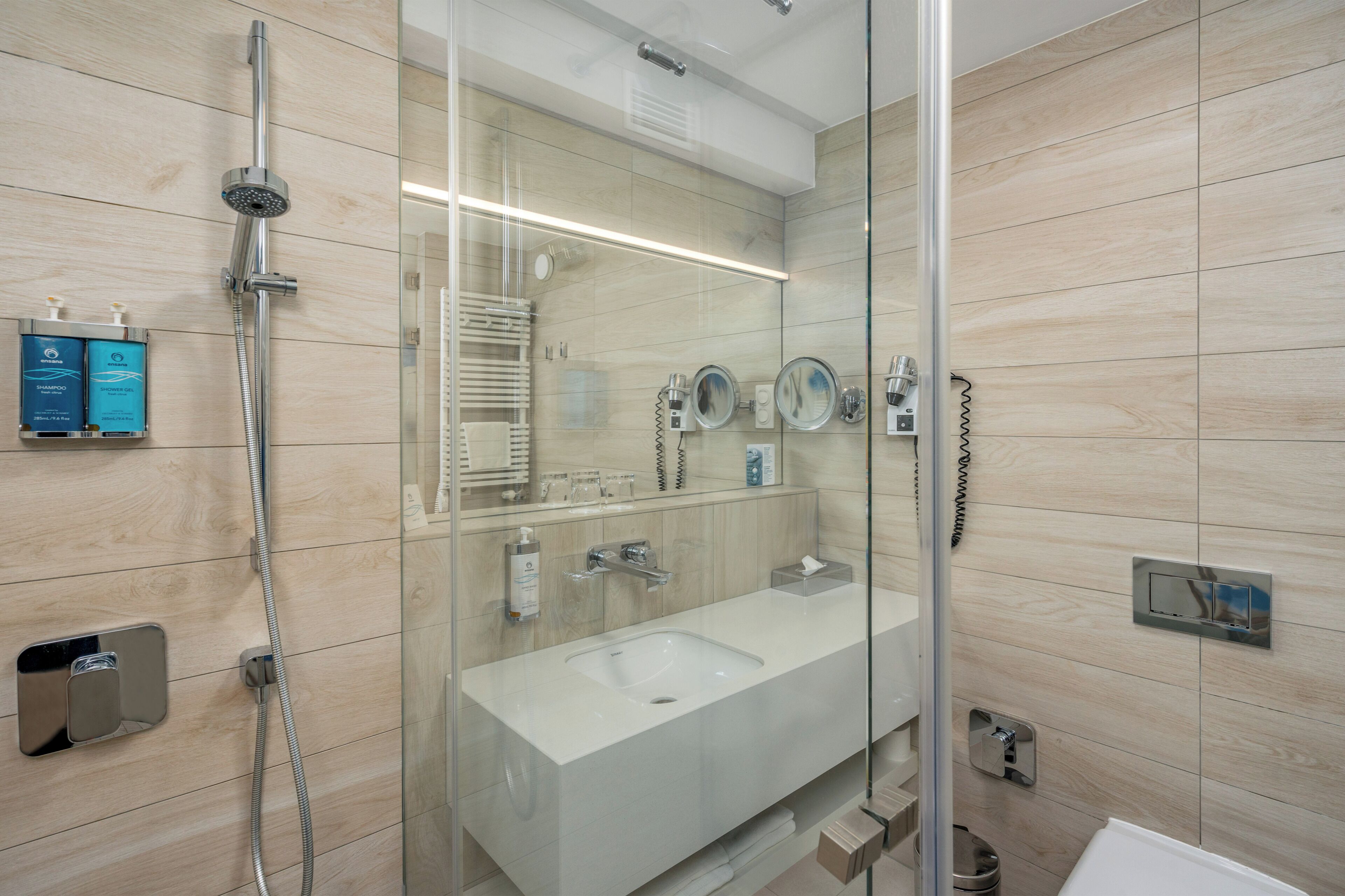 Ein modernes Badezimmer mit einer gläsernen Duschkabine, einem großen Waschbecken und einem Spiegel.