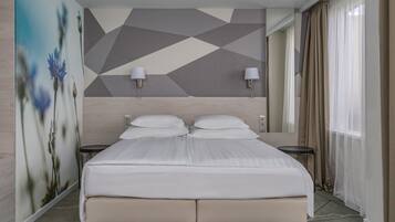 Una habitación de hotel moderna con una cama grande, dos mesitas de noche, un muro con estampado geométrico y un amplio ventanal con cortinas.