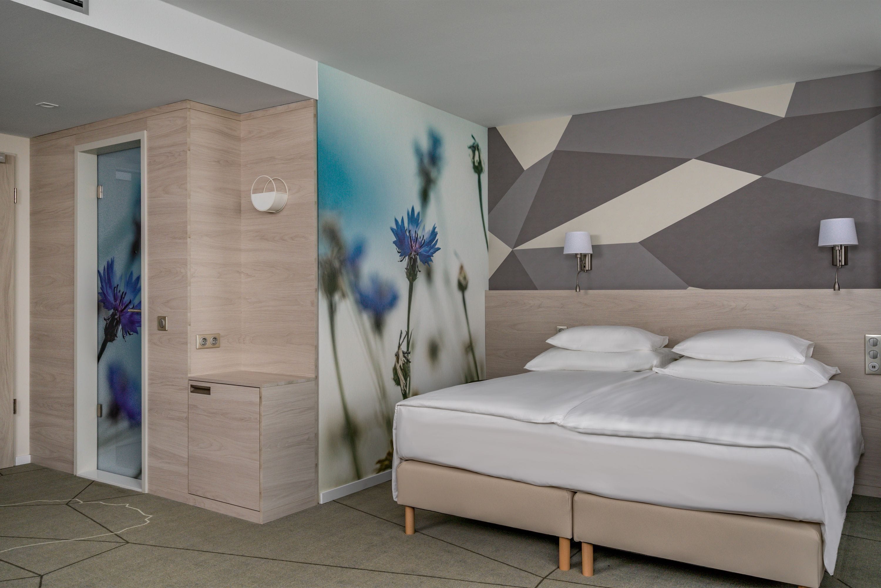 A modern bedroom with a bed, bedside lamps, and a wall with geometric patterns.