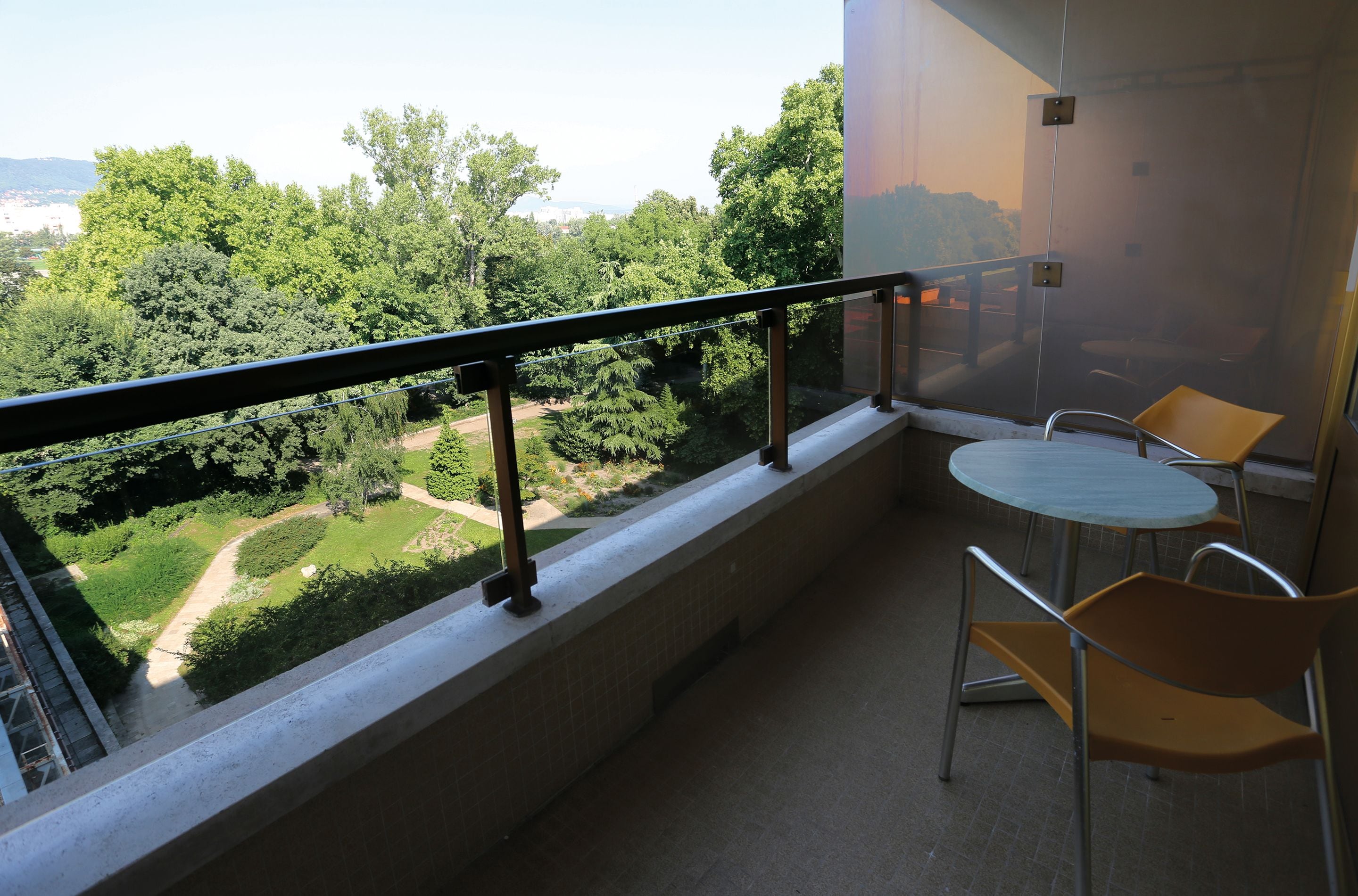 A balcony with a view of a green landscape, a small table, and two chairs.