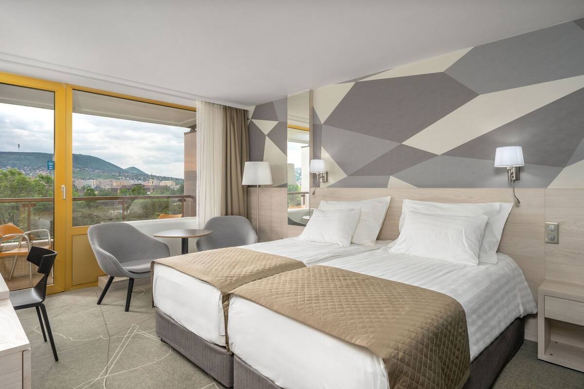 Ein Hotelzimmer mit Bett, Nachttischen, Schreibtisch, Stuhl und Blick auf die Stadt.