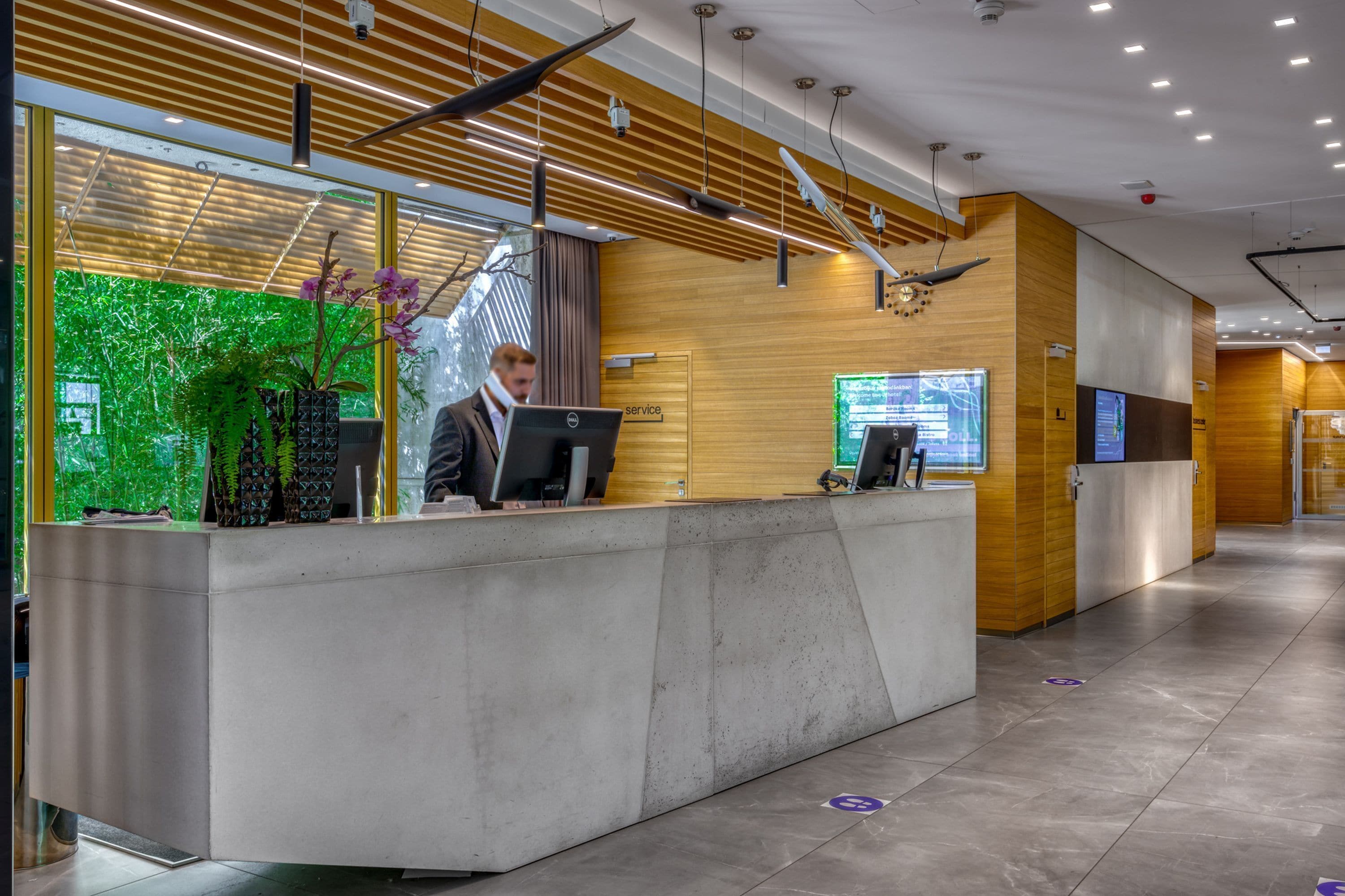 En moderne receptionsdisk med træpaneldesign, en digital skærm og en potteplante.