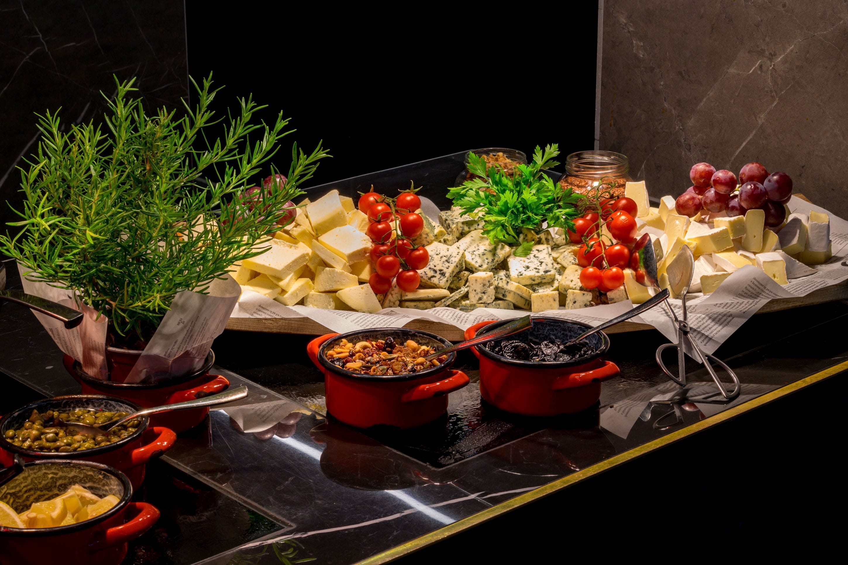 A buffet with various cheeses, tomatoes, and a potted plant.