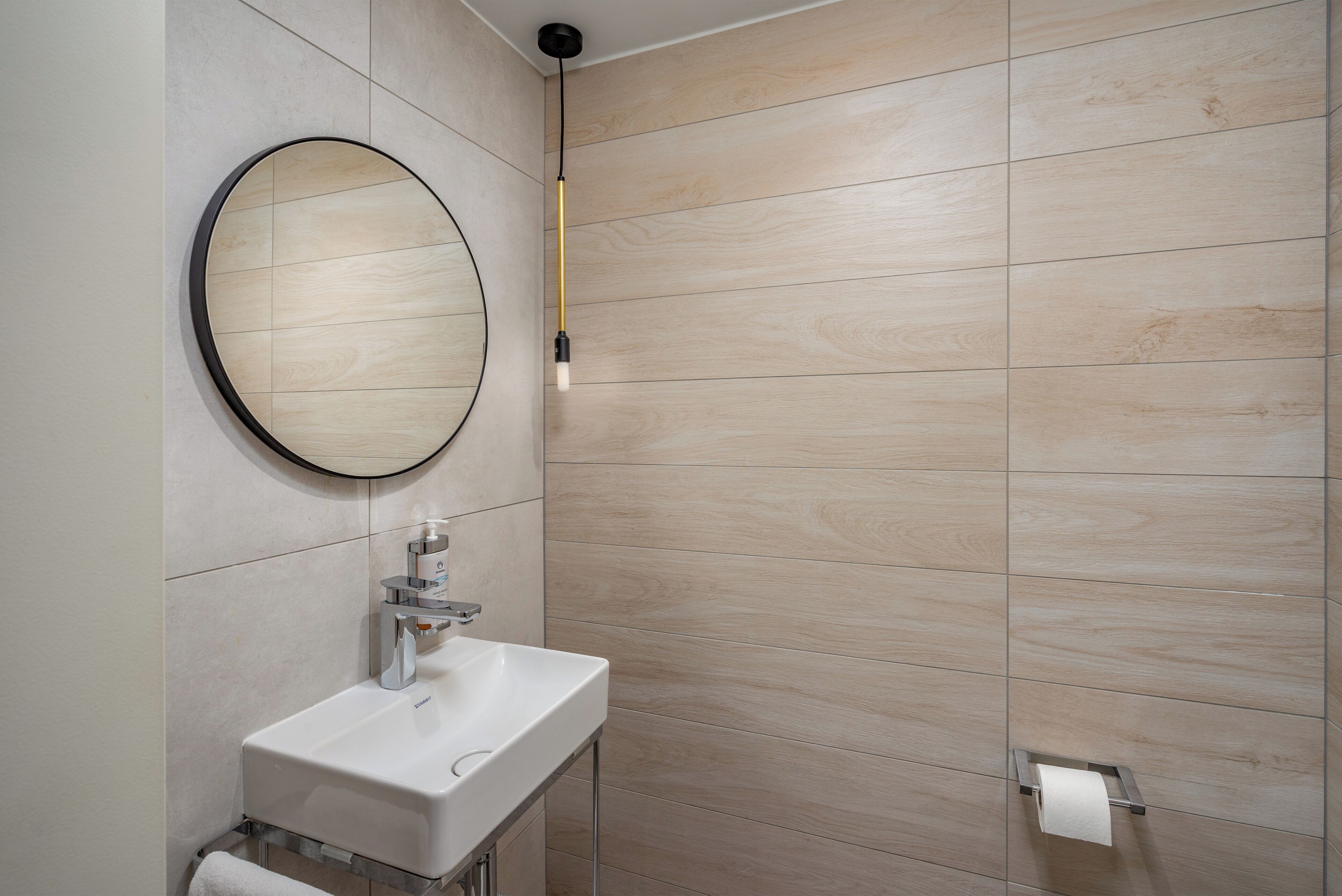 A bathroom with a round mirror, a white sink, and a toilet paper holder on the wall.