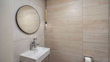 A bathroom with a round mirror, a white sink, and a toilet paper holder on the wall.