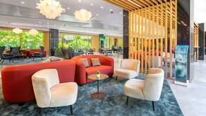 A modern lobby with a red sofa, white armchairs, and a small table with a plant. - Ensana Thermal Margaret Island (Budapest)