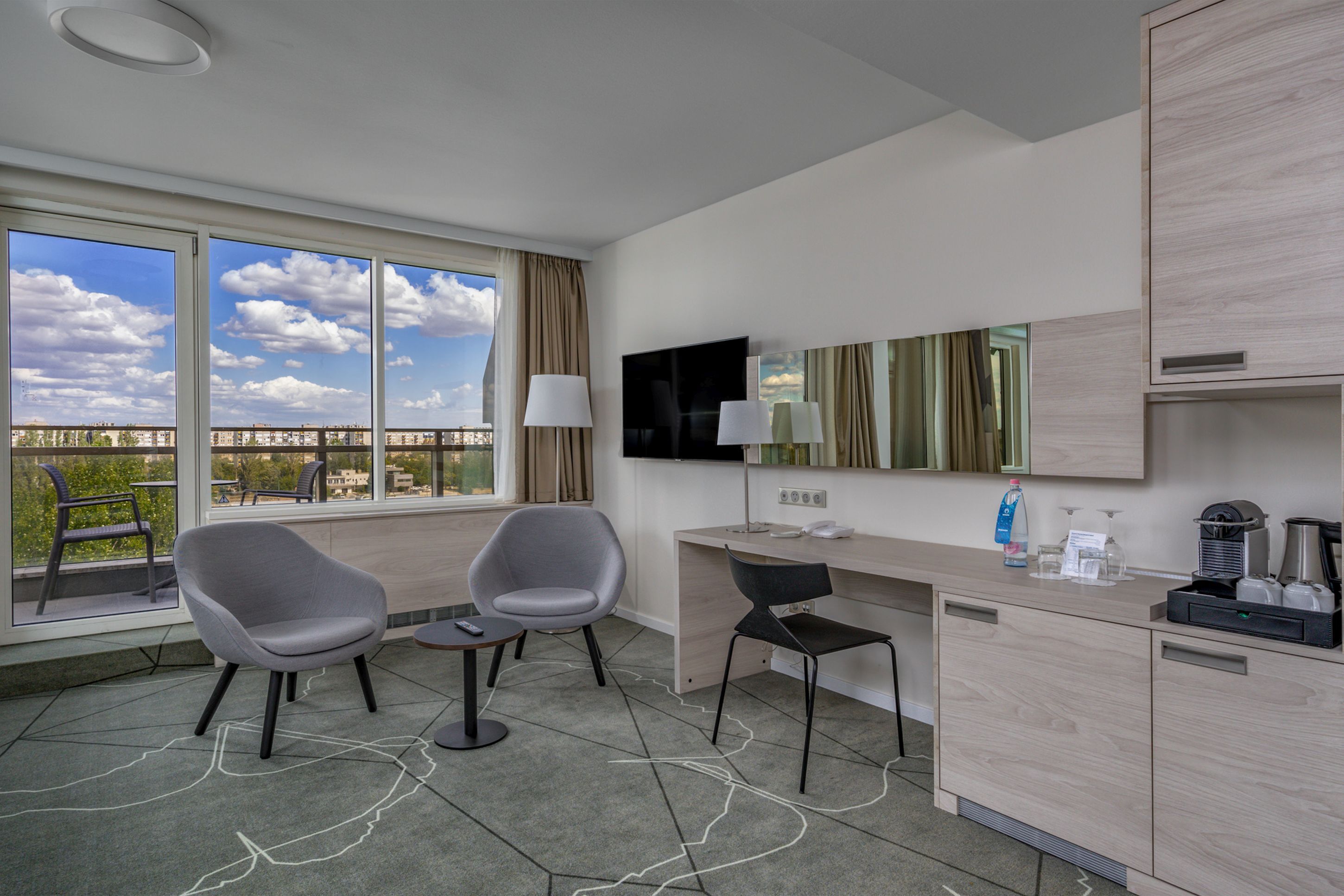 Habitació d'hotel moderna amb escriptori, dues cadires, televisió i una finestra gran que dona a una vista de la ciutat.