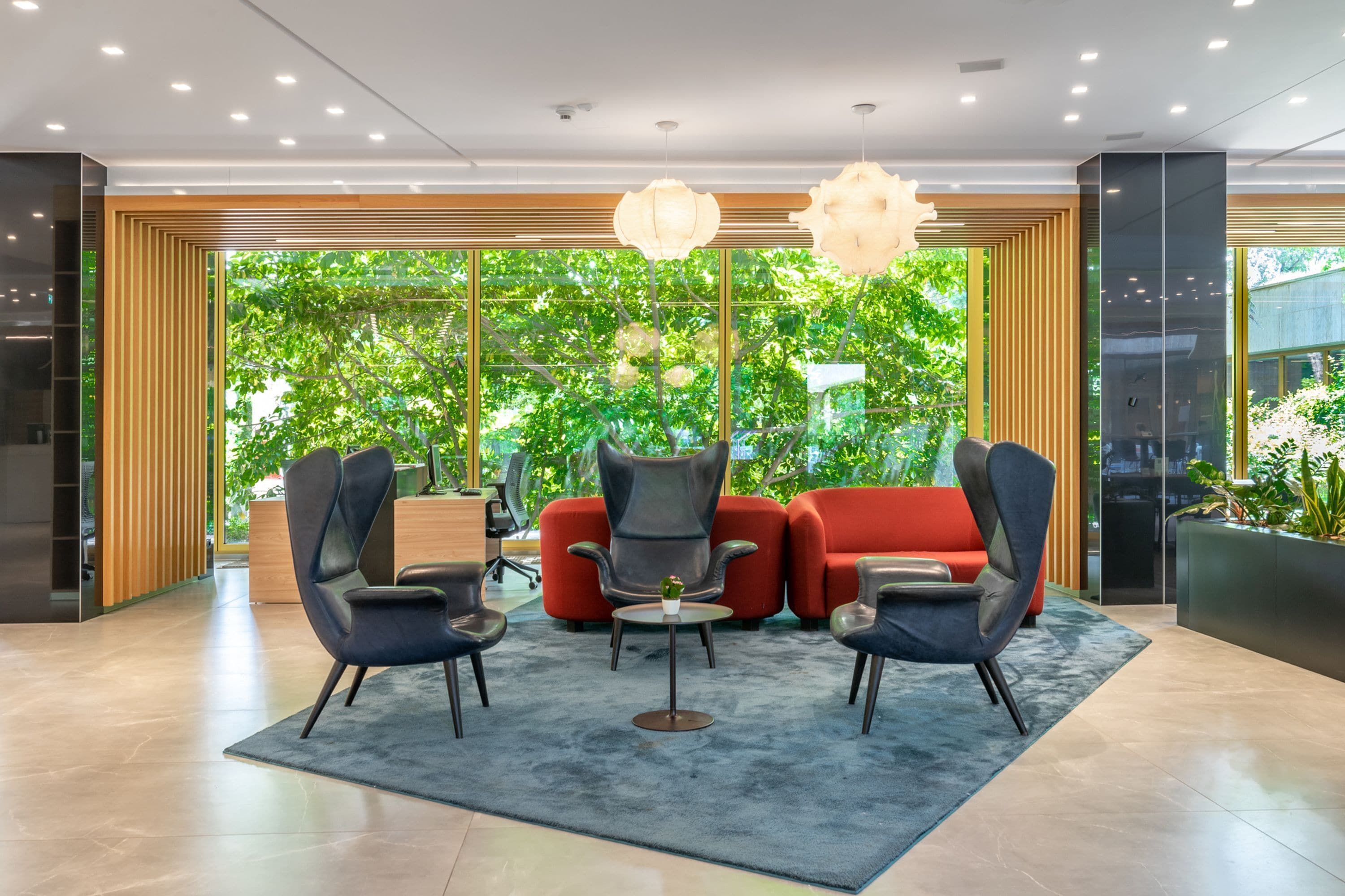 Een moderne lobby met een rode bank, zwarte stoelen en een kleine tafel met een plant.